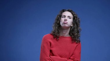 Kadın derinden iç çekmekten sıkılmış kollarını kavuşturmuş yukarı bakıyor ve can sıkıntısı içinde mavi arka planda duruyor.