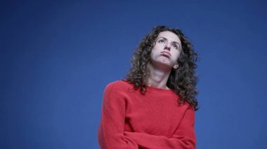 Kadın derinden iç çekmekten sıkılmış kollarını kavuşturmuş yukarı bakıyor ve can sıkıntısı içinde mavi arka planda duruyor.