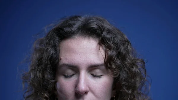 Young woman close-up eyes in meditation and contemplation on blue backdrop. Detail face of person introspecting and opening eyes feeling relaxed