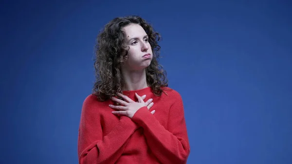 Young woman feeling relief by putting hand on chest, taking a deep breath of relaxation after struggle standing on blue background
