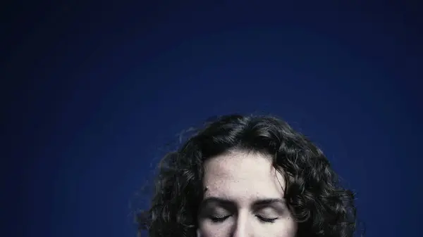 Young woman closing eyes in meditation and relaxation on blue backdrop, person forehead with top space of screen available for animation