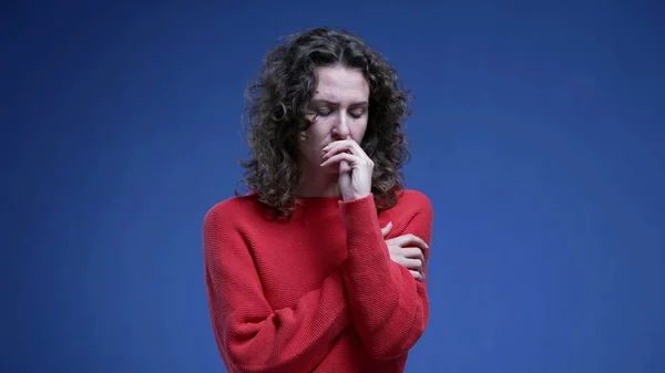 Anxious young woman biting nail in fear and nervousness. 20s female person feeling scared and fearful standing on blue backdrop