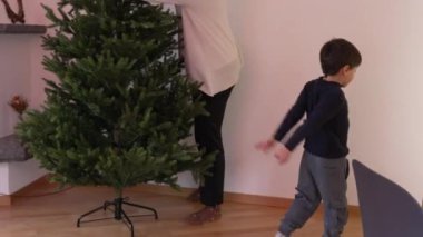 Anne, çocuk oynarken Noel ağacı kuruyor. Aile hazırlama şenliklerinin olduğu sıradan bir bayram sahnesi.