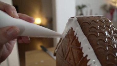 Zencefilli kurabiye evini dekore eden, ev yapımı Noel aşçılığı sanatının üstüne kraliyet buzu koyan birinin makro yakın plan fotoğrafı.