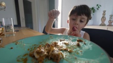 Küçük çocuk yemek masasında çatal kullanarak yemek yiyor.