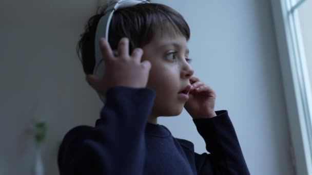 Jeden Mały Chłopiec Słuchawkach Stojący Przy Oknie Zdejmuje Słuchawki Zastanawia — Wideo stockowe