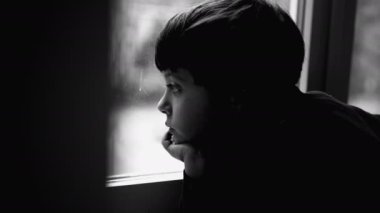Depresyondaki çocuk pencereden dışarı bakıyor, zihinsel hastalıkla boğuşurken, çocukluk depresyonu siyah beyaz, tek renkli, düşünceli genç bir çocukla tasvir ediliyor.