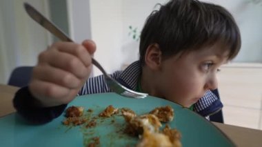 Düşünceli genç çocuk evde öğle yemeğinde lazanya yiyor. Düşünceli çocuk hayal kurarken çatal kullanarak yemeğin tadını çıkarıyor.