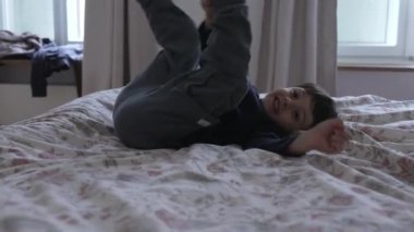 Enerjik çocuk yatakta zıplıyor, küçük çocuğun yatak odasında tek başına eğlenirken kaygısız hissi yatak çarşaflarında zıplıyor.