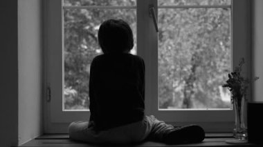 Hüzünlü çocuk, tek renk kıyafetle evinin penceresinden yağmuru seyrediyor. Kid 'in arkasında siyah beyaz depresyon var.