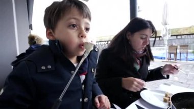 Anne ve çocuk tatildeyken restoranda İsviçre fondüsünün tadını çıkarıyorlar. Ekmeğe peynir üfleyen çocuğun yakın çekimi.