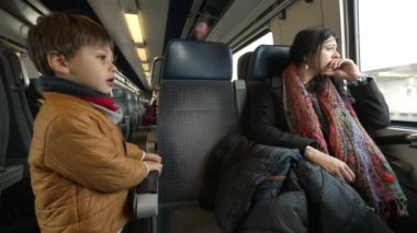 Anne ve çocuk trenle birlikte seyahat ediyor, küçük çocuk koridorda dikiliyor ve annesi Avrupa 'nın yüksek hızlı taşımacılığının içinden geçerken ona bakıyor.