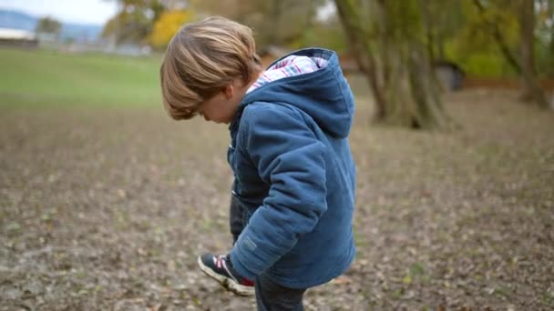 Маленький Мальчик Поднимает Ноги Проверяя Грязную Обувь Улице Парке Осенью — стоковое видео