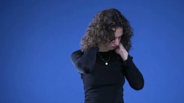 Stresli genç bir kadın mavi arka planda dururken zihinsel acıyı dindirmeye çalışıyor.