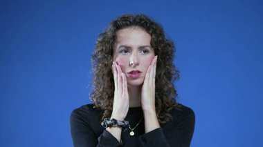 20 'li yaşlarda endişeli bir kadın endişeli ve kaygı dolu mavi arka planda düşünceli iç gözlemci bakışlarıyla duruyor.