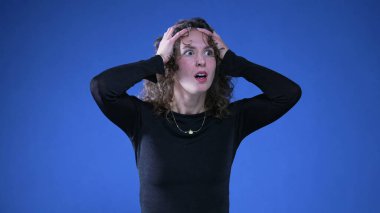 Endişeli kadın şok ve umutsuzlukla haberlere tepki veriyor kollarını başının üstüne koyuyor ve ağzı inançsızlık ve şaşkınlıkla örtüyor.