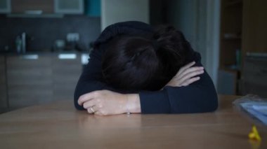 Evde oturan bunalmış kadın kendini yanmış ve depresif hissediyor. Masada yüzünü kapatan kişi zor zamanlarda depresif ve umutsuz hissediyor.
