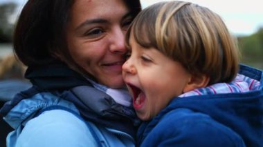 Küçük çocuk annesini yanağından öpüyor gerçek ebeveyn ve çocuk ilişkisinde. Aile hayatı için güzel bir an.