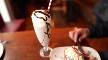 Lokantada şekerli yemek yiyip içen biri. Adam milkshake içer ve bir tabak krep yer.