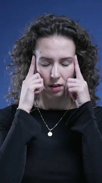 Stressed woman feeling mental pressure by pressing temples with hands trying to relax and take a deep breath during difficult times, blue background