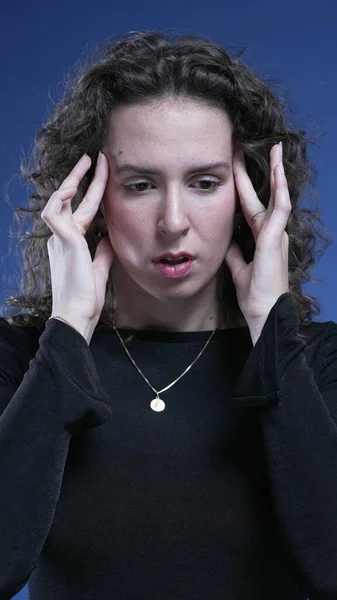 Stressed woman feeling mental pressure by pressing temples with hands trying to relax and take a deep breath during difficult times, blue background