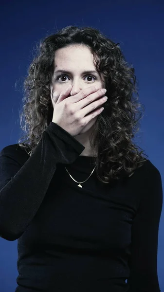 Woman covers mouth in SHOCK by news revelation, looking at camera feeling astonishment and SURPRISE