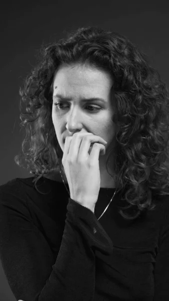 Despairing woman struggling with crippling anxiety by biting nails and ruminating past events in dramatic monochromatic, black and white