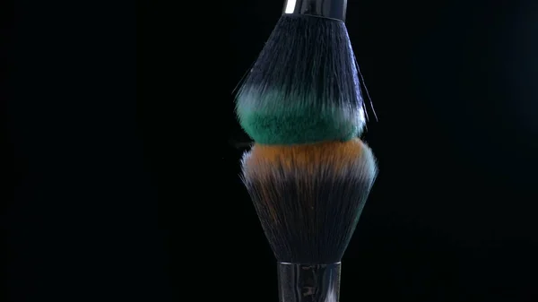 Cosmetic accessories brushing each other in super slow-motion at orange and green colors in black backdrop captured wiht high speed camera at 1000 fps
