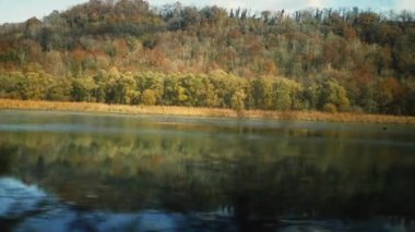 Trenin içindeki yolcu perspektifinden görülen doğal göl manzarası. Orman ve suyun güzel sonbahar günü