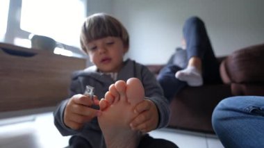 Oyuncu Çocuk ve Annesinin Evdeki Pedikür Zamanı, küçük çocuk isteksiz ebeveyni, ayak parmaklarını ve ayaklarını kesmeye çalışır.