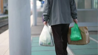 Banliyö çalışanı günlük rutin işlemler sırasında alışveriş torbaları taşır, plastik poşetlerle yürüyen adamın arkası.