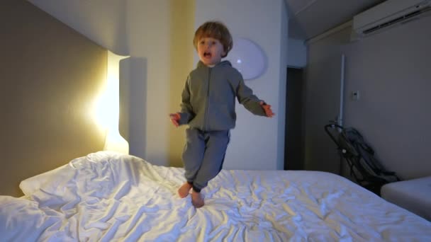 快乐的3岁小男孩在宾馆的床上蹦蹦跳跳 无忧无虑的兴奋孩子在床上跳来跳去 — 图库视频影像