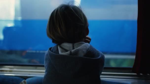 高速で鉄道のパスで並列列列車を見ながら列車の窓に傾いている思慮深い子供の背中 夢を見ながら旅をする子供 — ストック動画