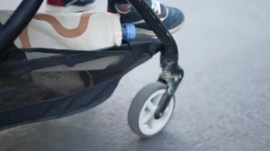Hareket halindeki bebek arabası asfalt kaldırımda bebek arabasını itiyor. Şehirde dolaşırken, çocuğun ayakları dışarıda sallanıyor.