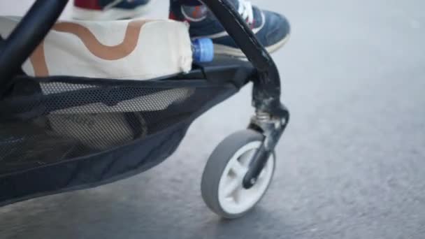 動作中のコントローラー アスファルトサイドウォークで赤ちゃんのキャリッジを押す 街を散策しながら外にぶら下がっている子供の足 — ストック動画