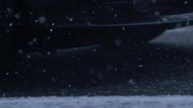 Winter snowfall on asphalt road while car passes in background in slow motion captured in 1000 fps