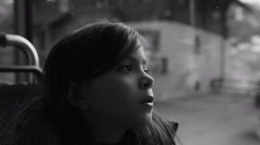 Passenger child travels by bus looking at scenery pass by in black and white, monochromatic clip of thoughtful small girl