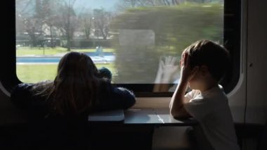 Kids sitting by train window, little brother covering face and eyes from sun rays while traveling with sister. Family on vacation