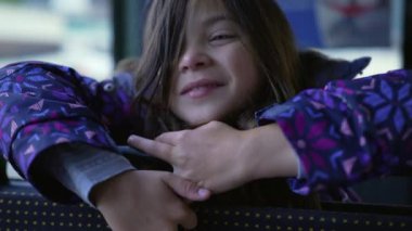 Closeup of a pensive happy little girl face leaning on bus seat smiling. Thoughtful 8 year old child