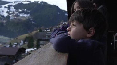 Tahta alp alp alp balkonuna yaslanan çocuk kış mevsiminde dağ manzarasına bakıyor, aile İsviçre Alplerinde tatilde.