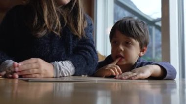 Restorandaki çocuklar menüden yemek topluyor, 8 yaşındaki küçük kız kardeşinin yanındaki seçeneği işaret ediyor.