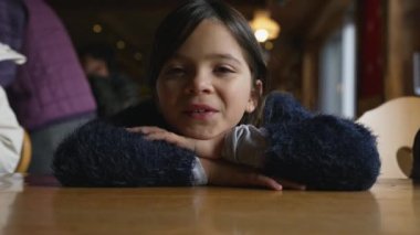 Masaya yaslanıp kameraya bakan mutlu küçük bir kız. Restoranda 8 yaşındaki çocuğun gülümsemesi.