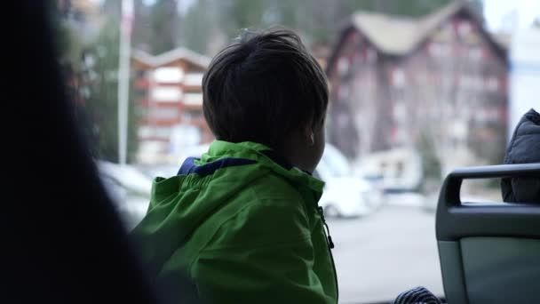 孩子们穿着雨衣从公共汽车窗口的座位上观察城市 乘客小男孩从公共交通工具上望出去 — 图库视频影像