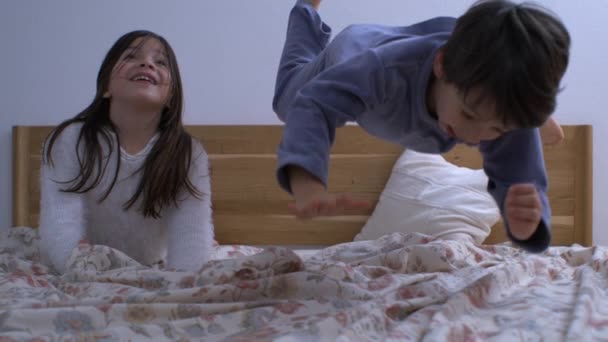 姐妹俩笑的时候 弟弟在床上跳的快乐时刻 在超级慢动作中捕捉的快乐家庭生活时刻 — 图库视频影像