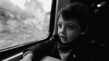 Trenle seyahat eden çocuk, pencere kenarından geçen, tek renkli, siyah beyaz manzarayla yakalanmış.