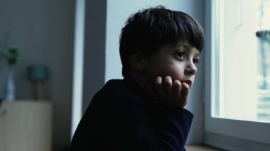 Düşünceli, sıkkın bir çocuk, evde el pençe divan durup, iç içe düşünceli bir ifadeyle apartman penceresinden manzarayı izliyor.
