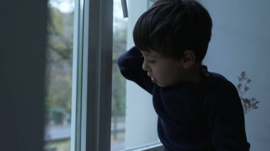 Sıkıcı çocuk evde sıkışmış, pencereye yaslanmış, evde sıkıntıyla boğuşan manzarayı seyrediyor.