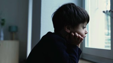 Düşünceli, sıkkın bir çocuk, evde el pençe divan durup, iç içe düşünceli bir ifadeyle apartman penceresinden manzarayı izliyor.