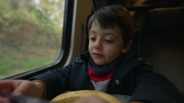 Düşünceli çocuk pencerenin kenarında oturmuş manzarayı seyrediyor. Kış mevsimi boyunca ceketi ve atkısı olan genç çocuk yüksek hızlı bir taşımacılıkla seyahat ediyor.