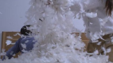 Küçük kız havaya bir sürü tüy atıyor. 1000 fps 'te süper yavaş çekimde çekiliyor. Kardeşi arka planda kardeşinin kuş tüyü kumaşıyla oynamasını izliyor.